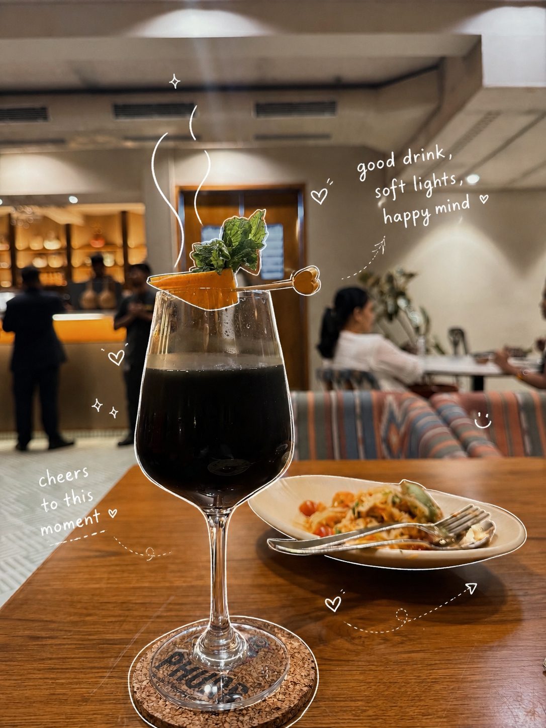Dark cocktail with mint and orange garnish in warm restaurant light