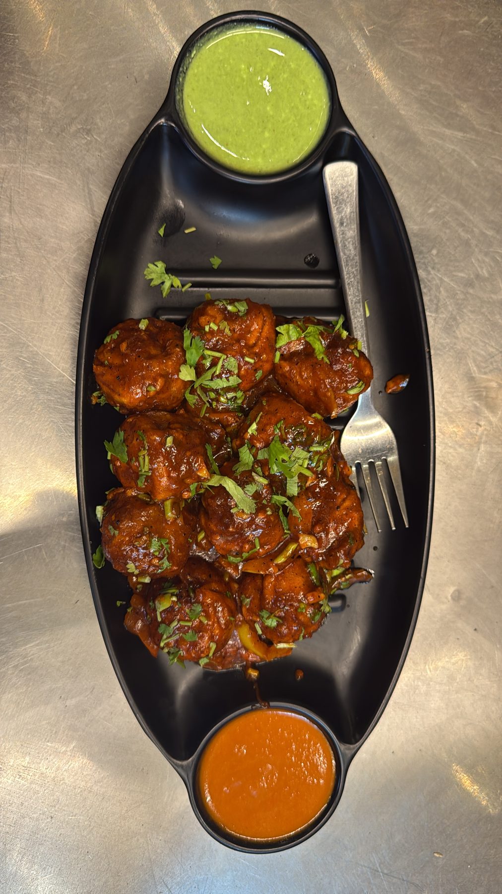 Fried dumplings in glossy sauce on a black boat platter