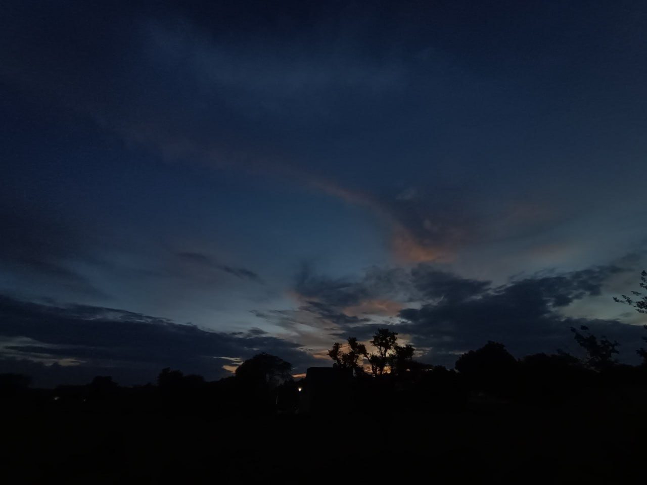 Indigo twilight sky with wispy clouds over dark rooftops