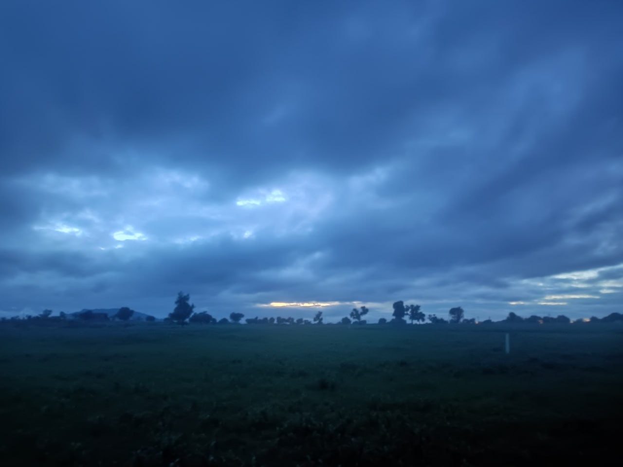 Open field under heavy clouds at dusk with a band of golden light