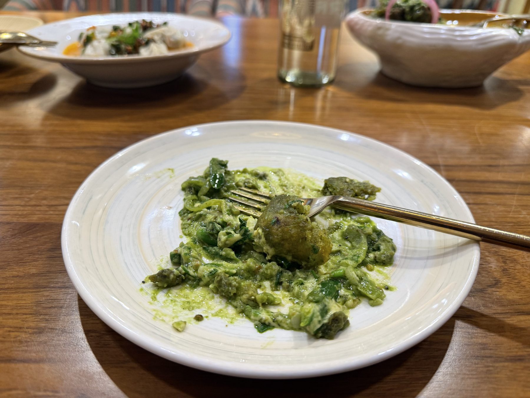 Green pesto gnocchi on a white plate with a fork lifting one dumpling