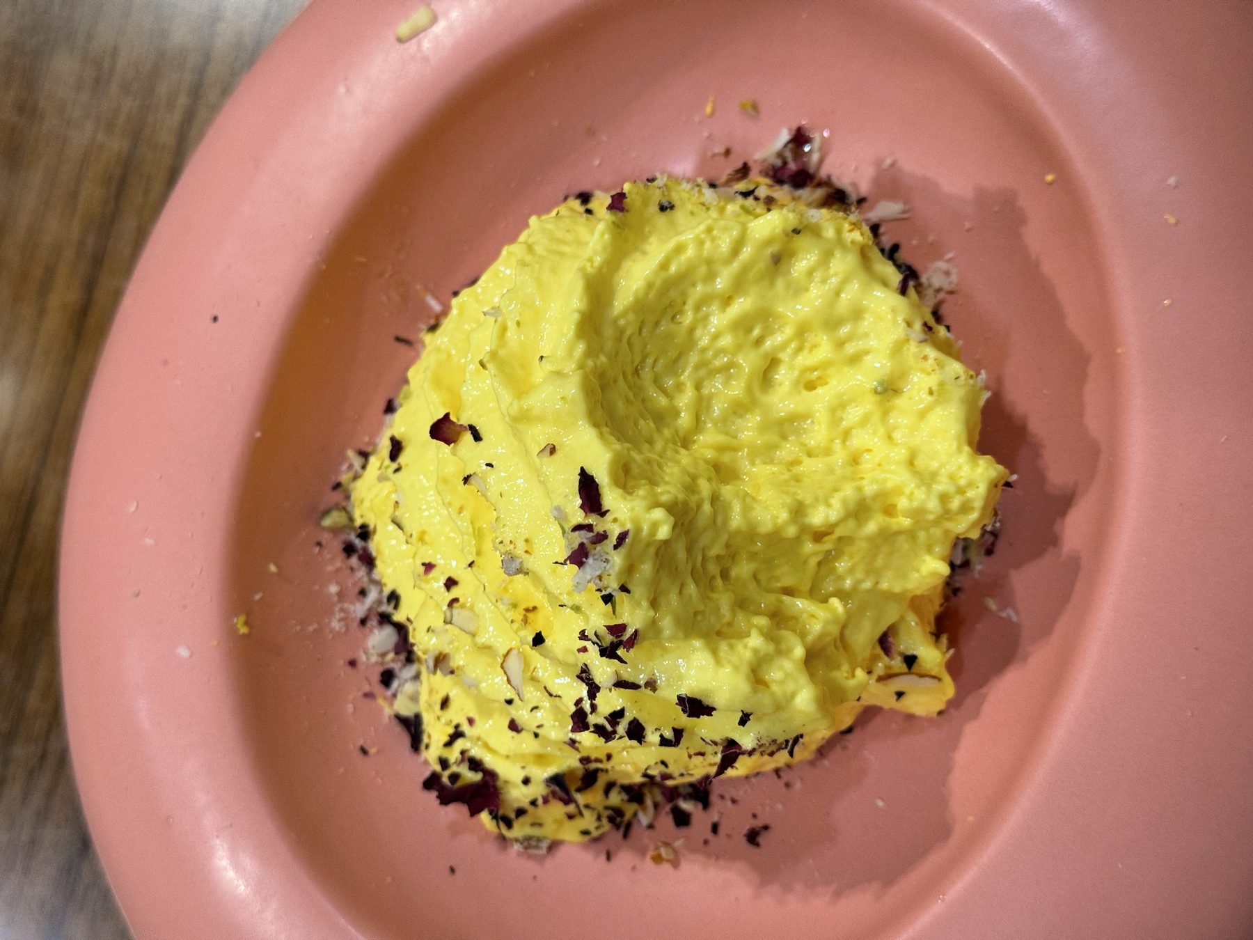 Thick yellow saffron dessert topped with rose petals in a pink bowl