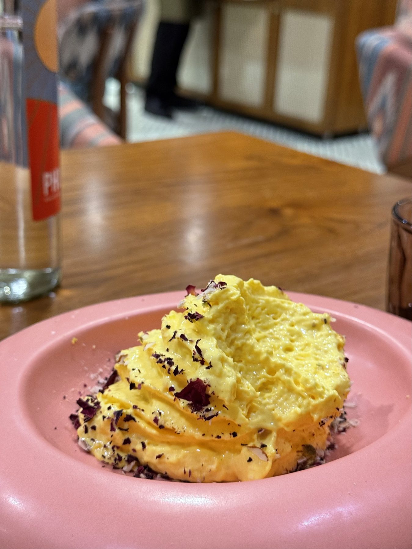 Yellow cream dessert with rose petals in a pink bowl