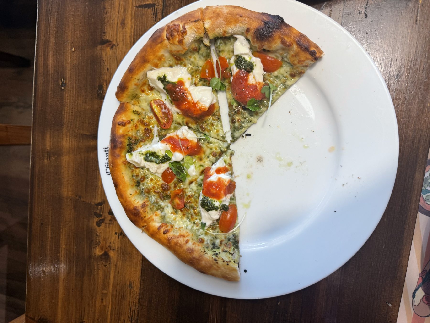 Partially eaten pesto and burrata pizza with cherry tomatoes
