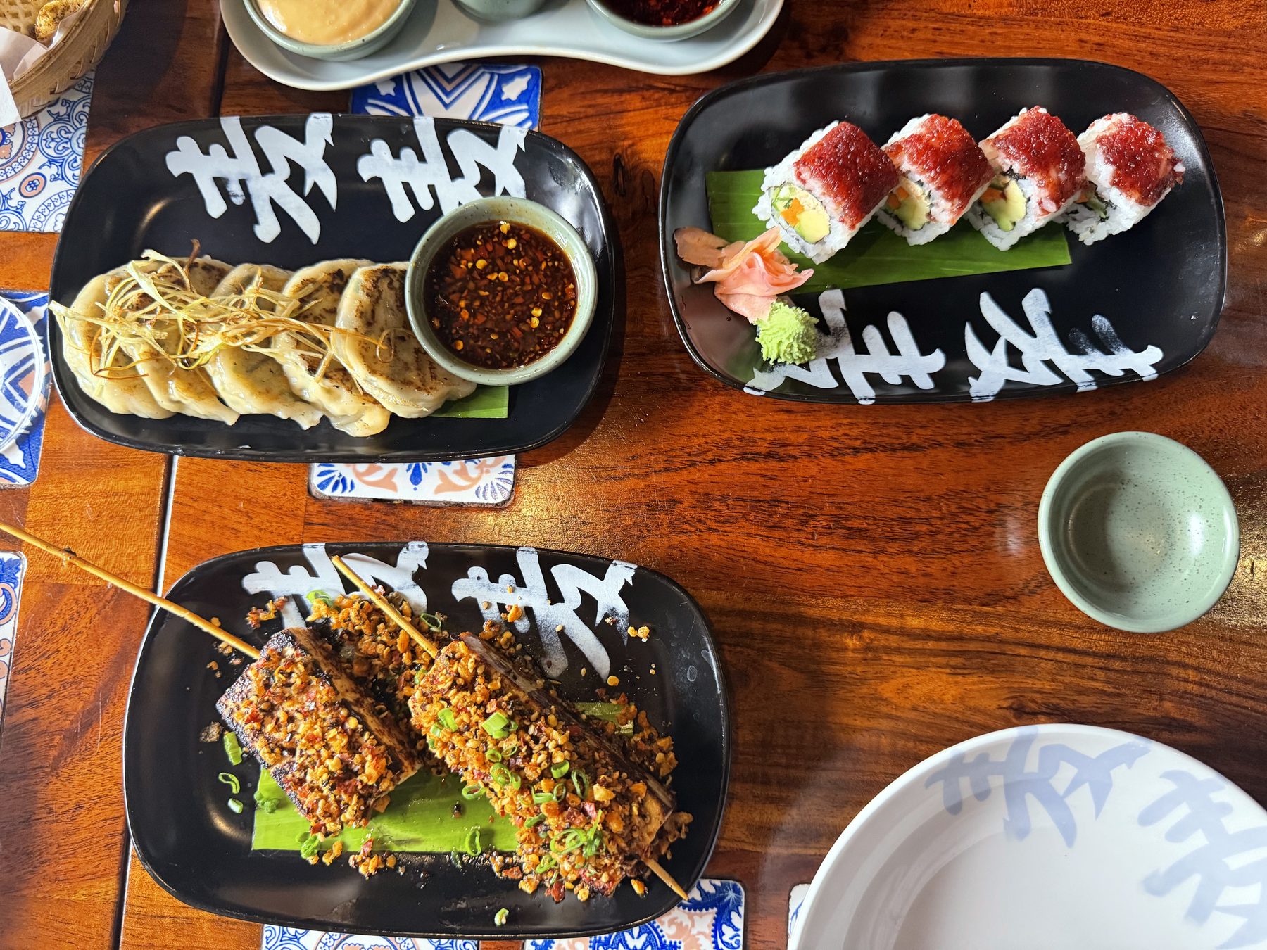 Gyoza, sushi rolls, and grilled skewers on black plates