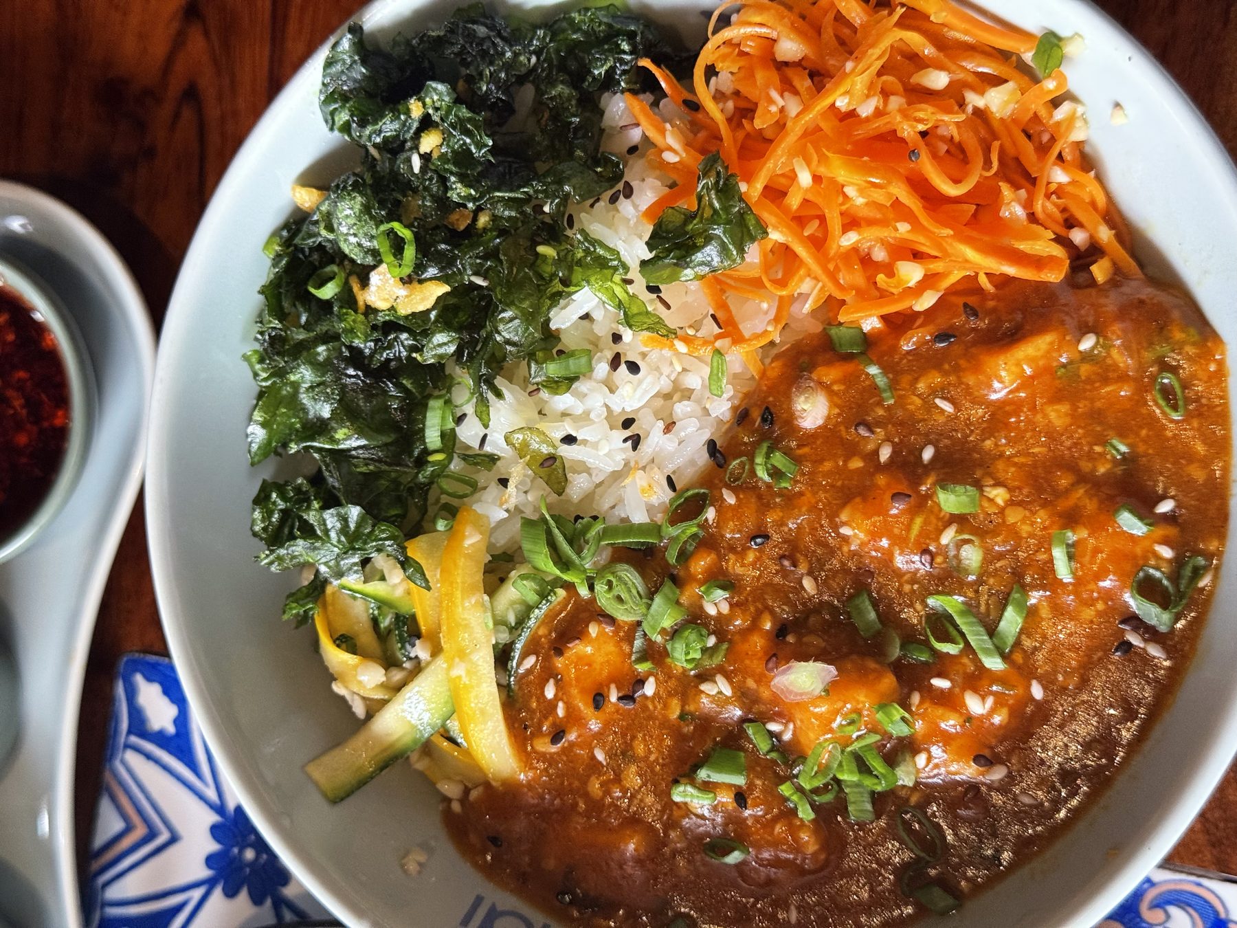 Colorful rice bowl with red sauce, greens, and shredded vegetables