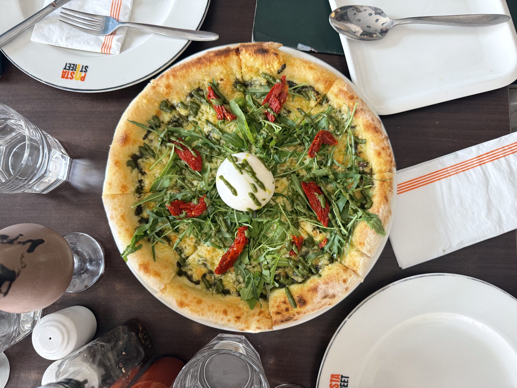 Pizza topped with arugula, sun-dried tomatoes, and whole burrata