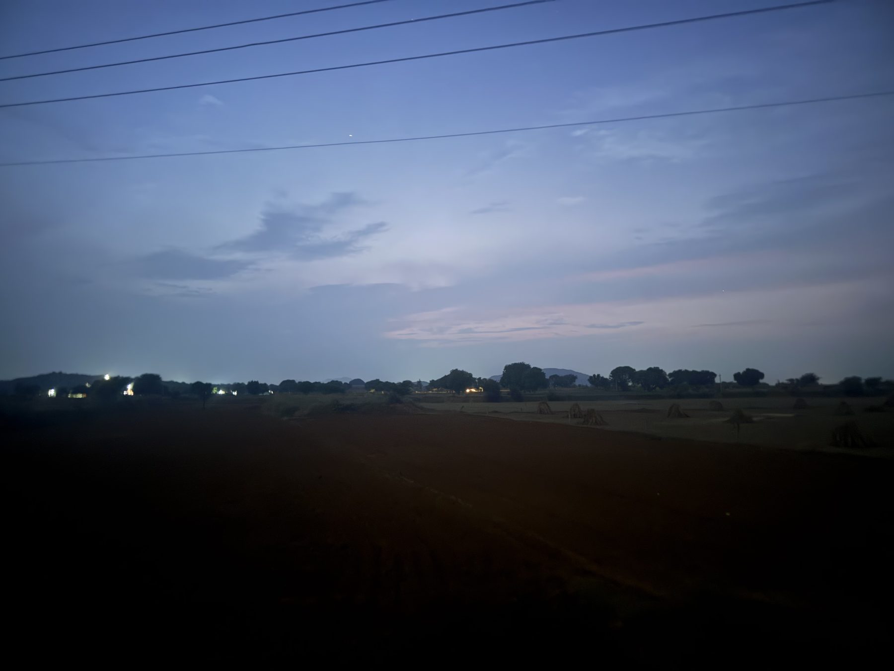 Rural landscape at dusk with pink-blue sky and distant village lights