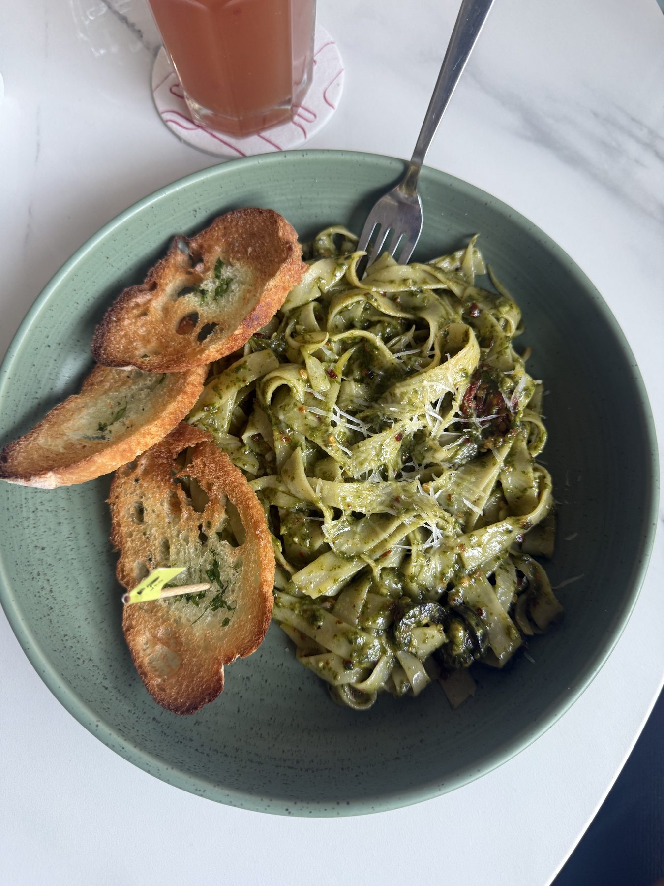Green bowl of pesto pasta with toasted baguette and pink juice