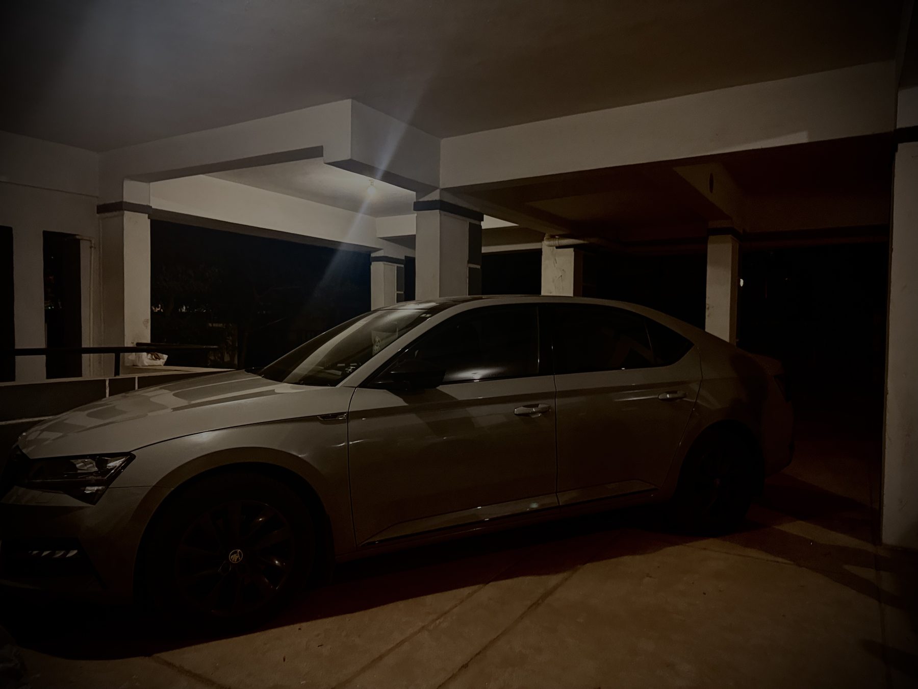 Silver sedan parked under concrete at night with dramatic lens flare