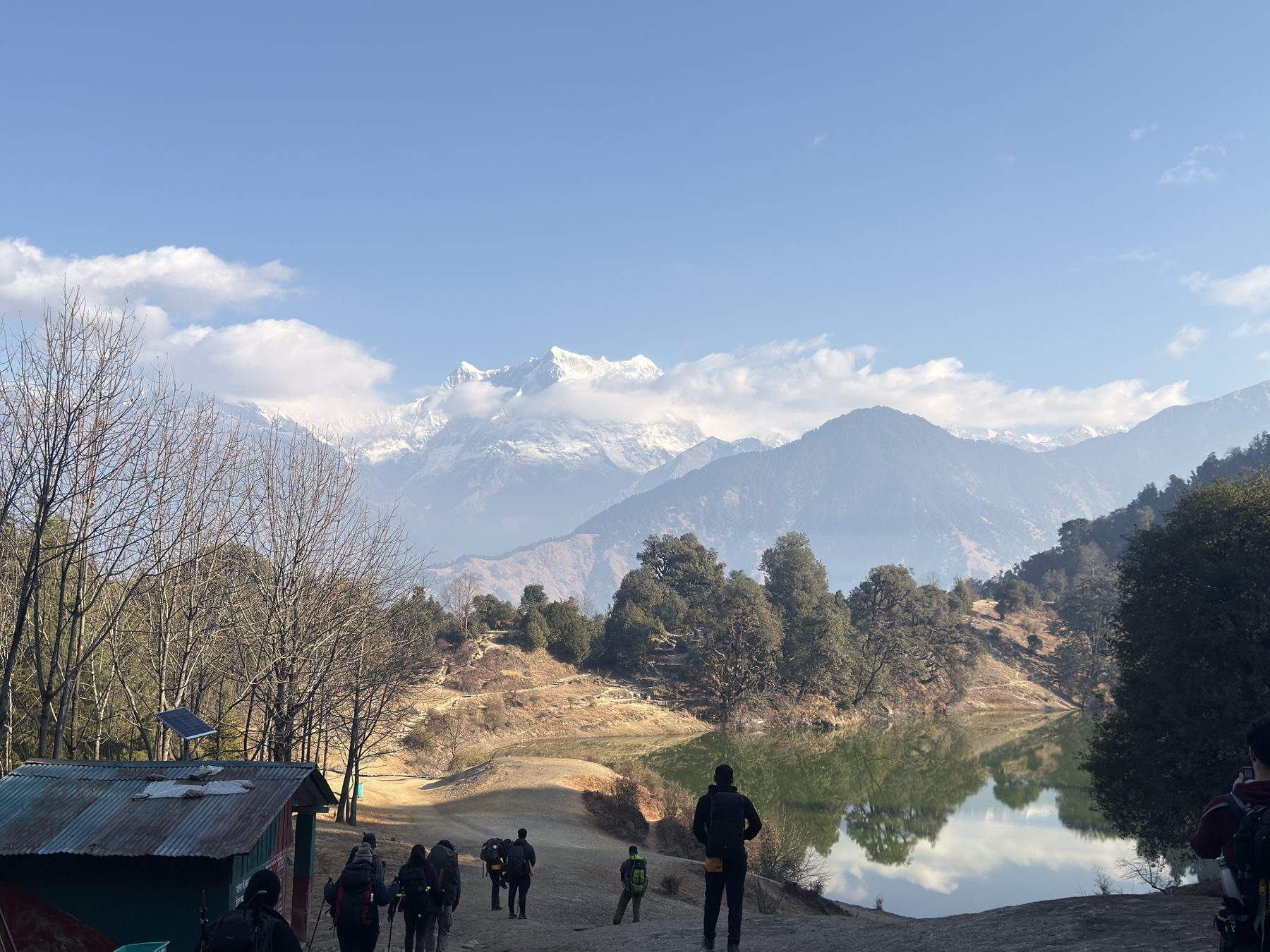 Trekkers on a ridge overlooking a still mountain lake and snow peaks