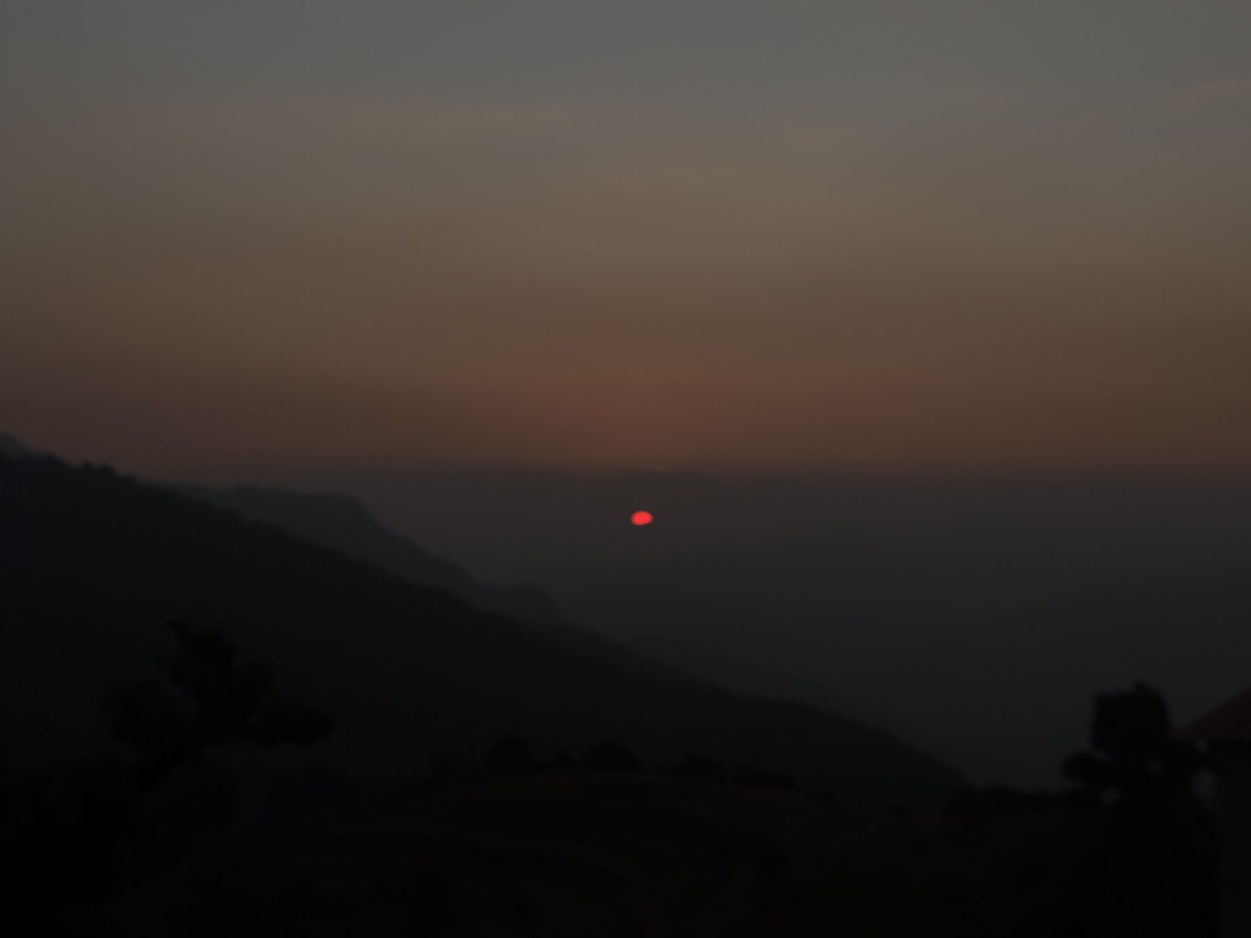 Small red sun above a hazy horizon between mountain ridges
