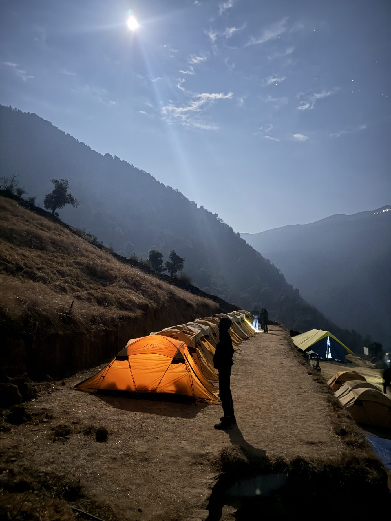 Orange tents along a mountain ridge under a bright moon