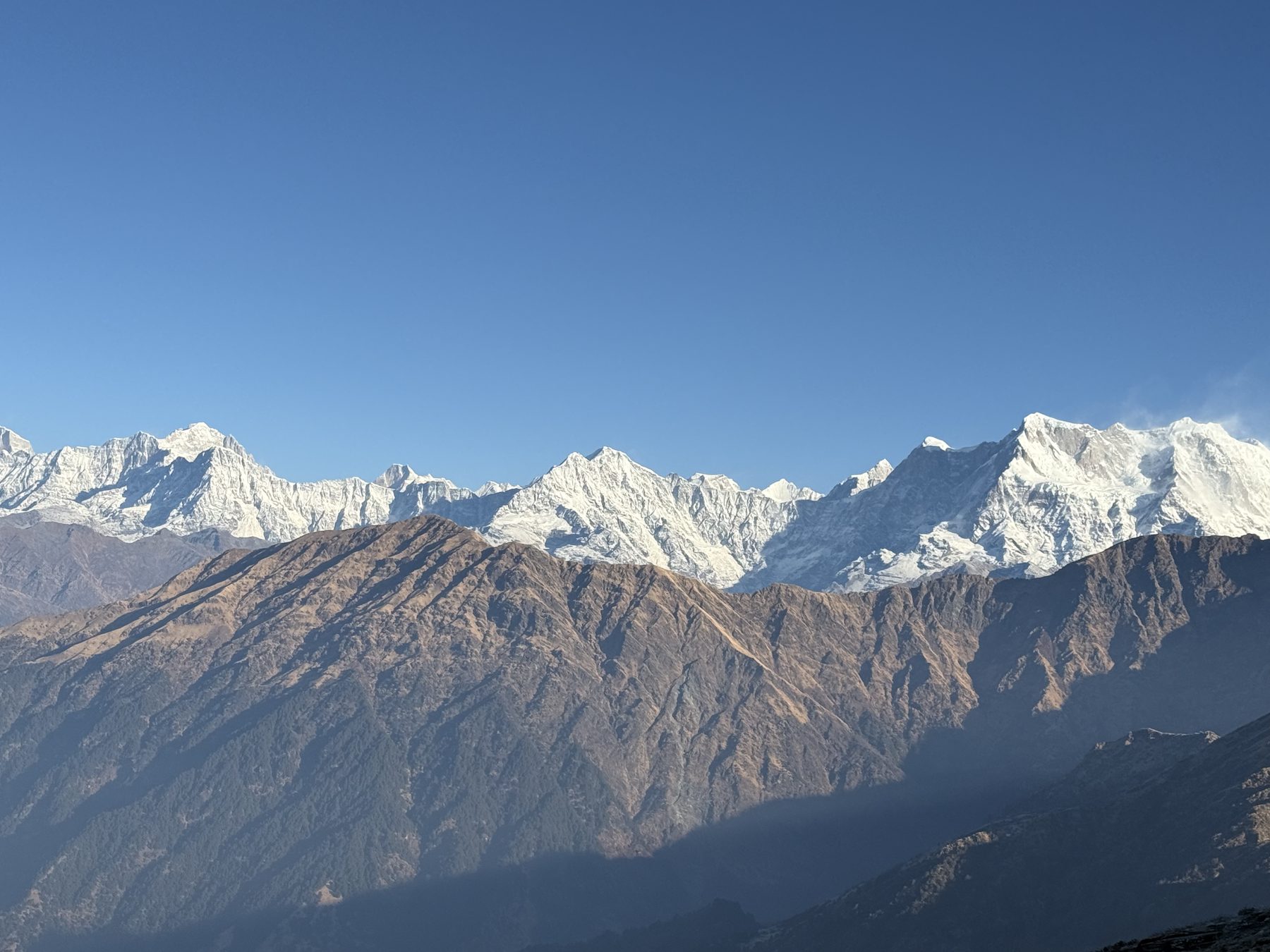 Rocky ridges rising toward jagged snow peaks under blue sky